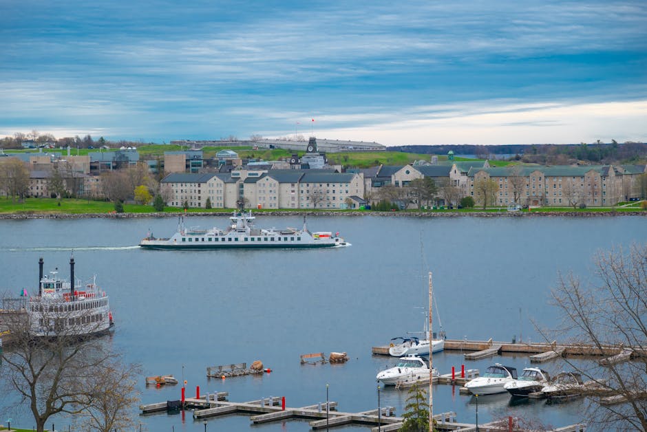 A cityscape featuring a variety of historic and modern buildings, with a prominent large white domed structure topped by a cupola located centrally in the background. In the foreground, out-of-focus purple and pink flowers partially obscure the view, adding a natural element to the scene. To the left, a grey stone building with decorative molding is visible, while on the right, a red-brick building with arched windows and detailed facades stands adjacent. The sky is partly cloudy with patches of blue, providing natural daylight that enhances the architectural details. The scene appears to be set in an urban area, possibly near a public square or street, with some pedestrians and seating visible at a distance, suggesting an active environment. This image could relate to independent waste collection or on-site clearance services by Rubbish Removal Kingston, especially in visualising the contrast between urban development and efforts to manage waste or improve public spaces.